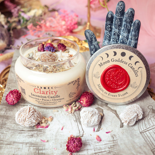 Clarity Intention Candle by Moon Goddess Candles, hand-poured in Brooklyn and topped with dried botanicals and herbs, surrounded by spiritual decor and textured floral accents to support focus, direction, and mental clarity.