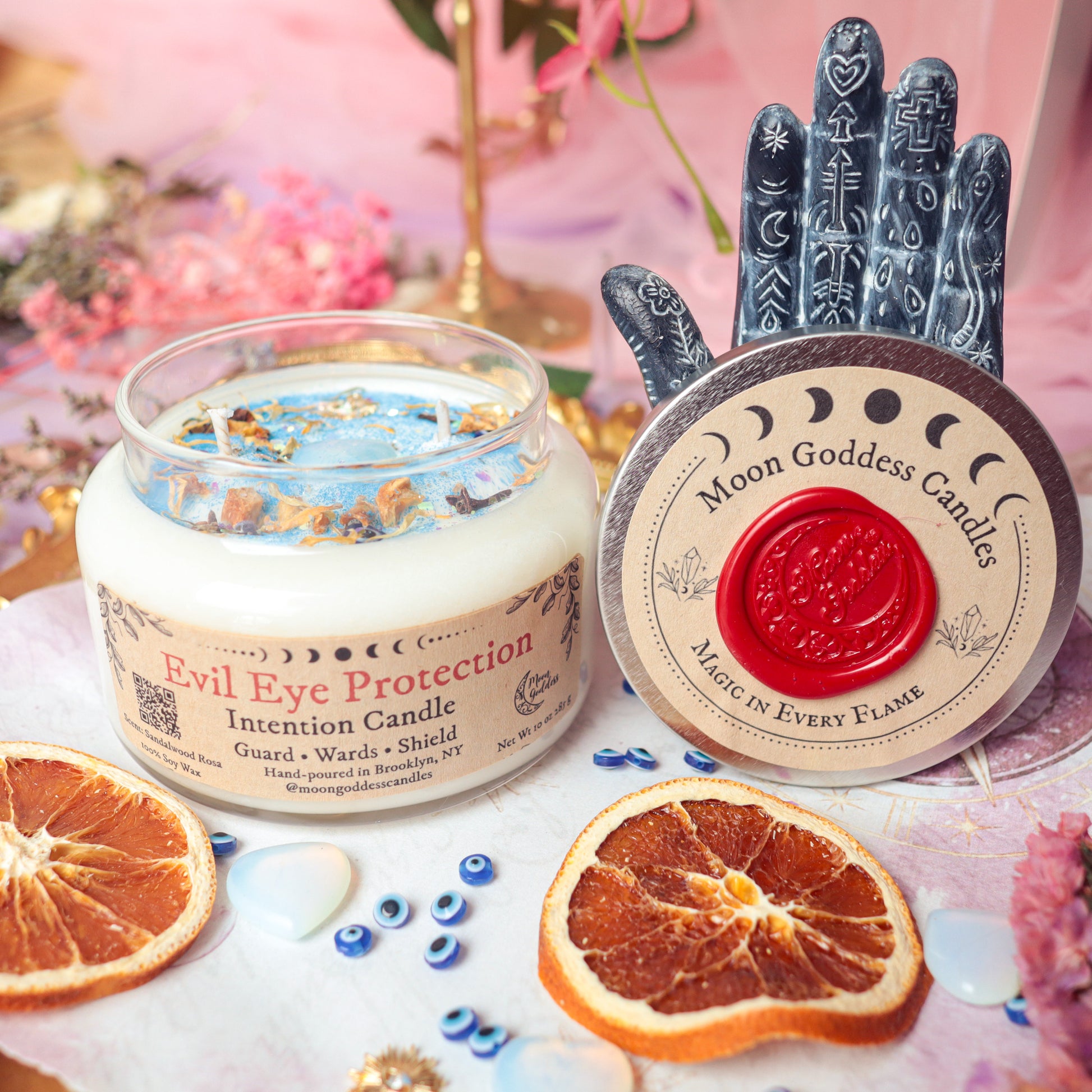 Evil Eye Protection Intention Candle by Moon Goddess Candles, hand-poured in Brooklyn with soy wax, dried herbs, and crystals, surrounded by dried orange slices and evil eye charms to guard, ward off negativity, and shield energy.