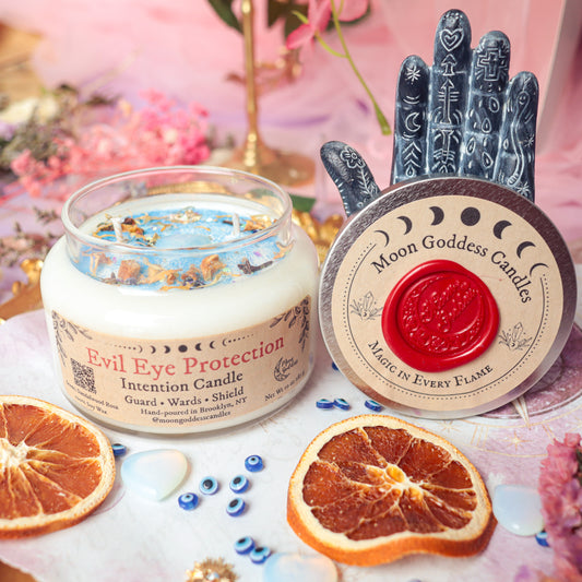 Evil Eye Protection Intention Candle by Moon Goddess Candles, hand-poured in Brooklyn with soy wax, dried herbs, and crystals, surrounded by dried orange slices and evil eye charms to guard, ward off negativity, and shield energy.