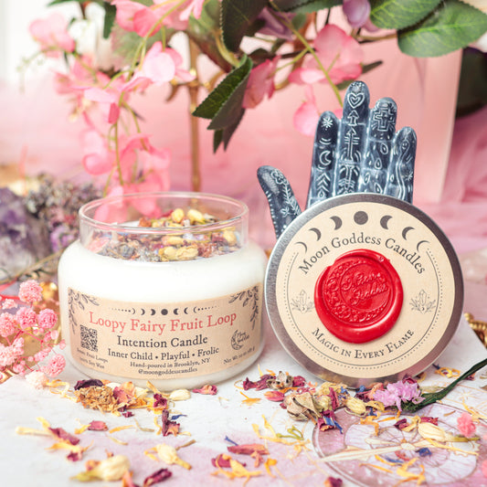 Loopy Fairy Fruit Loop Intention Candle by Moon Goddess Candles, hand-poured in Brooklyn and topped with colorful botanicals, surrounded by whimsical floral decor to spark inner child joy, playfulness, and magical frolic energy
